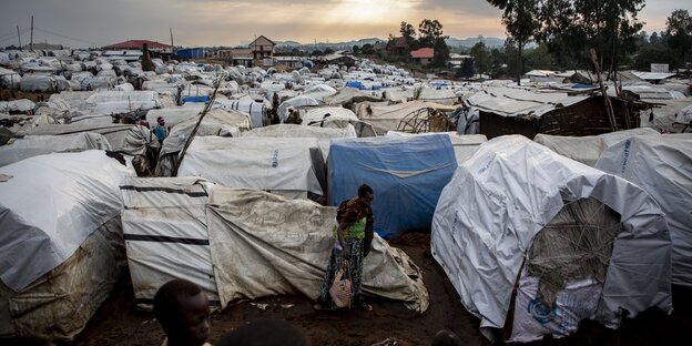 Sehr dicht gedrängt stehen die weißen Unterkünfte im Flüchtlingslager, eine Frau geht im engen Zwischenraum