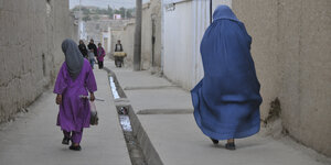 Neu errichtetr Weg mit einem Abwasserkanal in der Mitte, rechts eine Frau mit Burka und ein Mädchen im lila Kleid von hinten