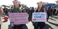 Zwei Demonstrantinnen mit Schweinemasken und Plakaten