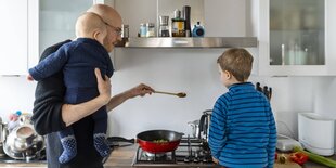 Ein Vater steht mit Baby und kleinem Jungen am Herd