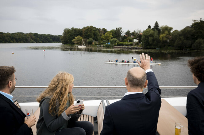 Scholz und andere von hinten auf einem Schiff, im Hintergrund ein Ruderboot