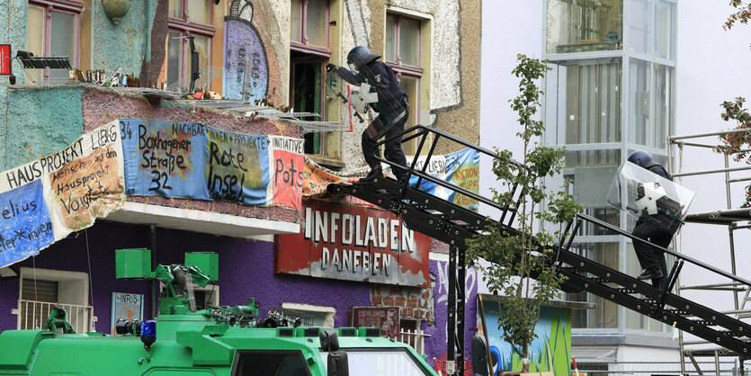 Polizisten steigen über einen Leiter durch ein Fenster in einem bunten Haus ein