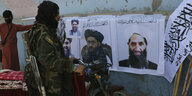 Ein Taliban-Kämpfer mit Waffen vor Plakaten mit Taliban-Führern