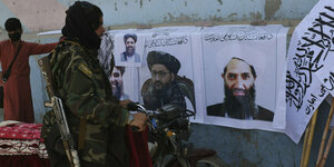 Ein Taliban-Kämpfer mit Waffen vor Plakaten mit Taliban-Führern