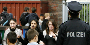 Polizist von hinten mit schwarzer Jacke neben Schülerinnen