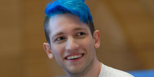 Der Youtuber Rezo mit blauen Haaren lächelt und schaut zur Seite