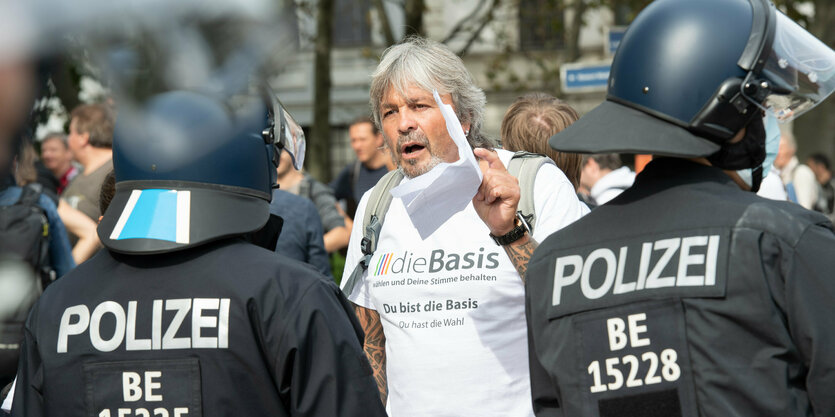 Ein Mann ohne Maske steht hinter einer Polizeireihe und gestikuliert wild