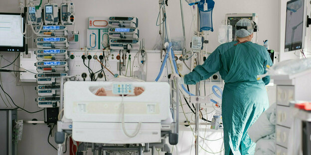 Eine Intensiv-Pflegerin in grünem Kittel steht neben einem Krankenbett