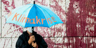 Mann mit blauem Schirm und der Aufschrift: Klimakrise steht - im Hintergrund die mit Kunstblut verzierte Fassade der CDU