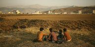 Vier junge Männer sitzen auf einem Feld, Im Hintergrund sind Häuser
