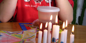 Ein Junge im roten T-Shirt sitzt vor sieben weißen Kerzen