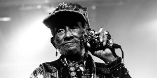 Le Scratch Perry am Mikrofon schmuckbehangen und einer geschmückten Kappe