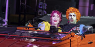 Die Sängerin Irene Roberts und der Sänger Dean Murphy sitzen mit bunten Perücken in einem Cabrio