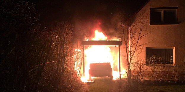Brennendes Auto und Carport neben einem Haus