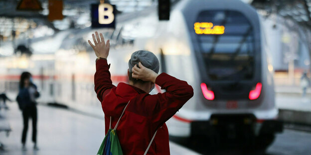 Eine Person auf einem Bahnsteig reckt die Hand in die Luft, im Hintergrund unscharf ein einfahrender ICE