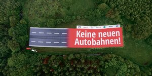 Ein Banner mit der Aufschrift "Keine neuen Autobahnen!", der einen Autobahnabschnitt darstellt, ist auf einer Landfläche zu sehen.
