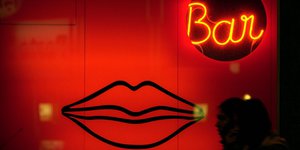 Rot beleuchtetes Schaufenster einer Erotikbar, Leuchtreklame mit Lippen und dem Schriftzug „Bar“