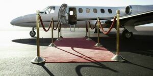 Ein Privatflugzeug steht mit geöffneter Tür auf dem Rollfeld, der Einstieg wird von einem roten Teppich gesäumt