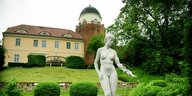 Eine renovierte Burg, davor ein Garten mit einer Frauenstatue