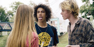 Samuel, Janik und eine junge Frau stehen zusammen im Freien. Samuel streckt seine Zunge raus und zeigt sein Zungenpiercing
