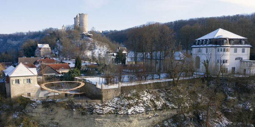 Blick auf leicht winterliche Landschaft, oben auf dem Hügel Ruine einer Burg, darunter das Giebelhaus der Werkstätten, daneben die schlaufenähnliche Brücke von Dorte Mandrup