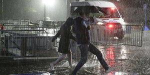 Zwei Fußgänger rennen durch den Regen mit Schirm
