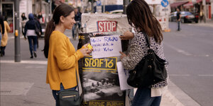 Zwei junge Frauen stehen in Berlin auf dem Gehsteig vor einem Aushang auf dem steht: „Hallo Rawad melde dich, du wirst Vater“