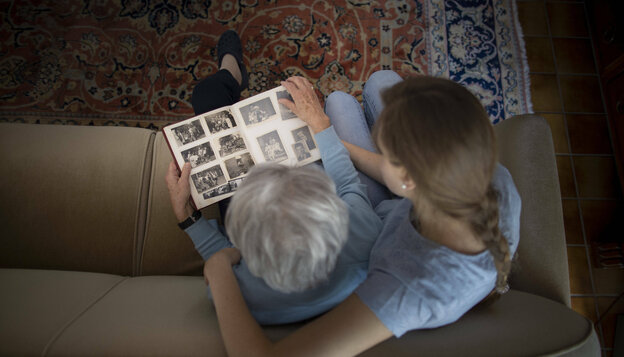 Eine Frau sitzt mit einer Seniorin auf dem sofa und sieht sich ein Fotoalbum an