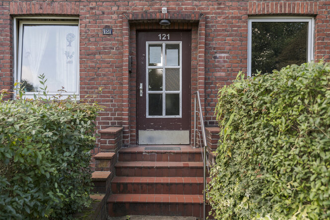 Ein paar Treppen hin zum Eingang eines Backsteinhauses, rechts und links der Treppe Büsche