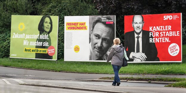Eine Person geht an Wahlplakaten von Annalena Baerbock, Christian Lindner und Olaf Scholz vorbei
