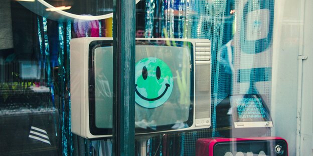 ein alter Röhrenfernseher im Schaufenster, auf dem grauen Bildschirm klebt ein grüner Smiley, der mehr gruselig als glücklich lächelt
