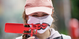 Demonstration gegen Stellenabbau: Eine Frau mit einer roten Ratsche in der Hand und einem Mund-Nasenschutz mit aufgemaltem unglücklichem Mund.