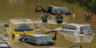 Mehrere Autos auf überfluteter Straße. Zwei Männer stehen bis zum Gürtel im Wasser