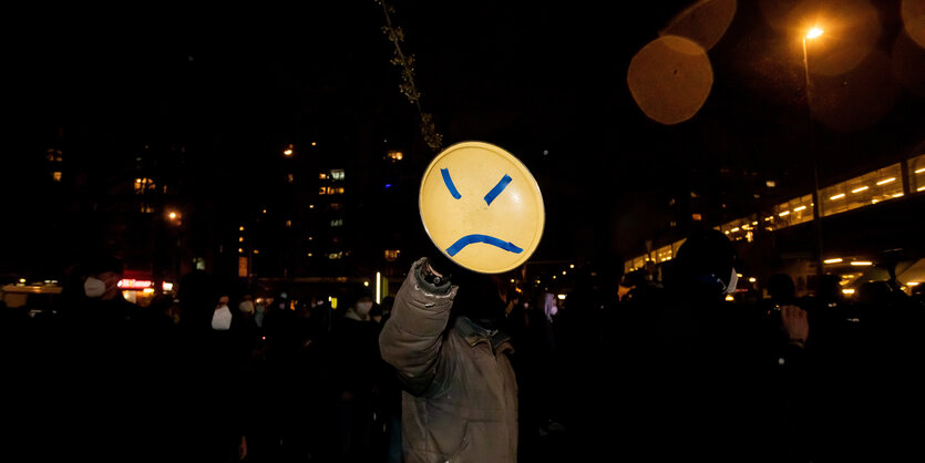 Person hält runde Pappe mit traurigem Smiley