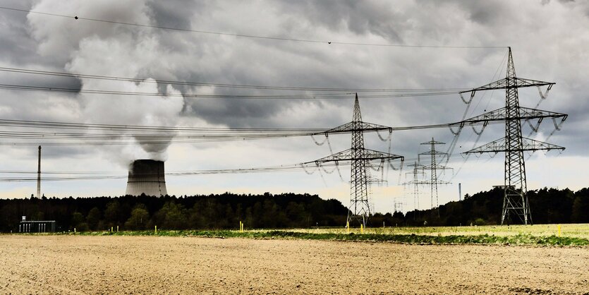 Der Turm des AKW Lingen ragt hinter Bäumen hervor. Daneben Strommasten und Leitungen