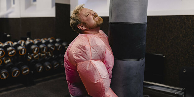 Ein Mann im Bodybuilderkostüm hantiert an einem Boxsack