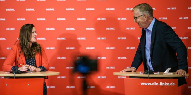 Janine Wissler und Dietmar Bartsche stehen an Pulten, dahinter eine rote Wand mit Schrift Die Linke