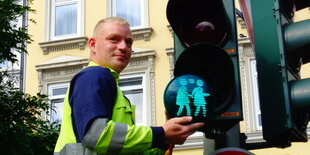 Mitarbeiter der Stadt bringt grüne Ampelplatten mit Pärchenmotiv an