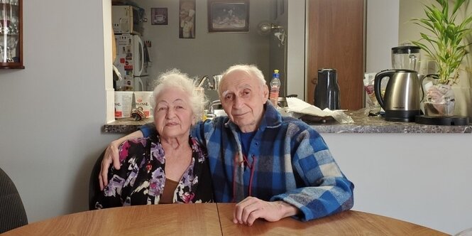 Efrem Steinbock umarmt seine Frau Geta beide sitzen am Tisch