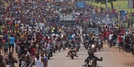 Jubelnde Menschenmeng auf Mopeds und zu Fuß begleitet Militärtransporter
