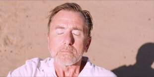 Tim Roth in der Sonne, rechts am Bildrand ist sein Schatten