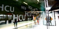 Personen stehen vor einer Glaswand mit Aufschrift HCU