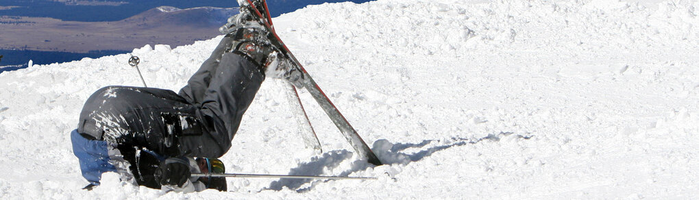 Ein Mensch mit Ski liegt im Schnee und Streckt die Beine nach oben