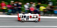 Eine Seifenkiste in der Form eines Stadtwerke Buses fährt bei einem Seifenkistenrennen auf einer Straße.