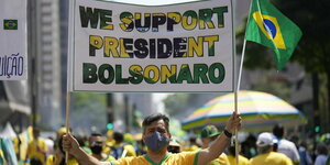Demonstranten in gelben Händen. Ein Mann hält ein Schild mit der englischen Aufschrift: Wie untersützen Präsident Bolsonaro