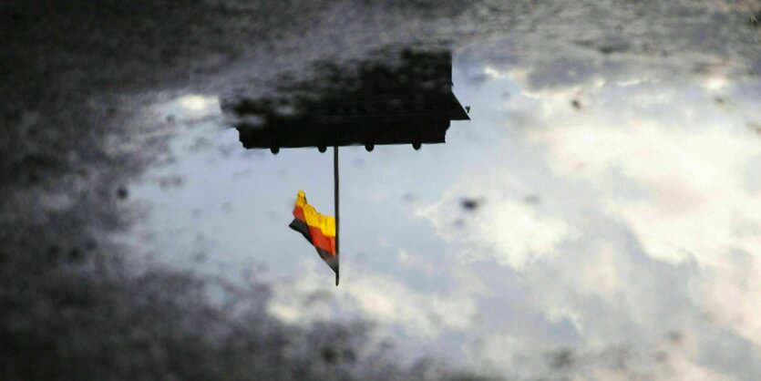 Die Deutsche Flagge auf dem Reichstag in der Reflektion in einer Pfütze