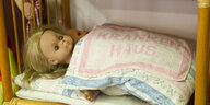 Eine Puppe liegt zugedeckt in einem Puppenbett