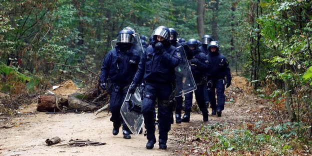 Vermummte Polizeitruppe mit Schildern und Helmen auf dem Weg zur Räumung im Hambacher Forst