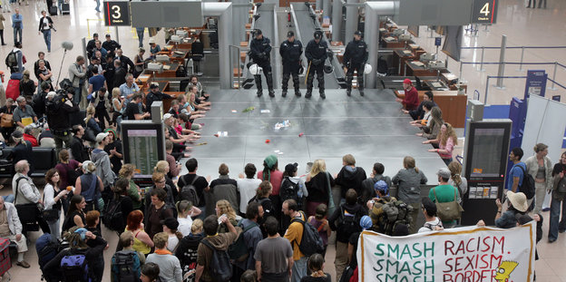 Polizisten stehen auf einem Flughafen Demonstranten gegenüber