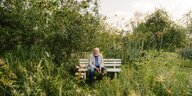 Succow sitzt auf einer Holzbank in einem grünen Garten